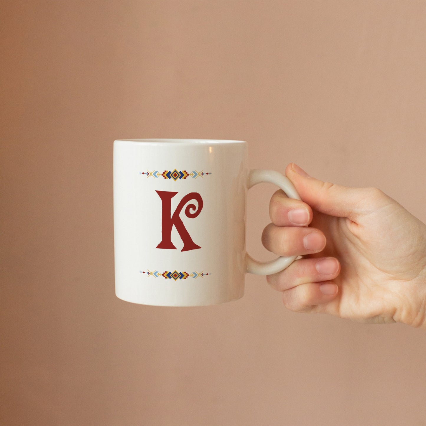 White mug with custom initial design held by a hand against a beige background