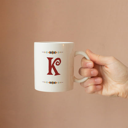 White mug with custom initial design held by a hand against a beige background